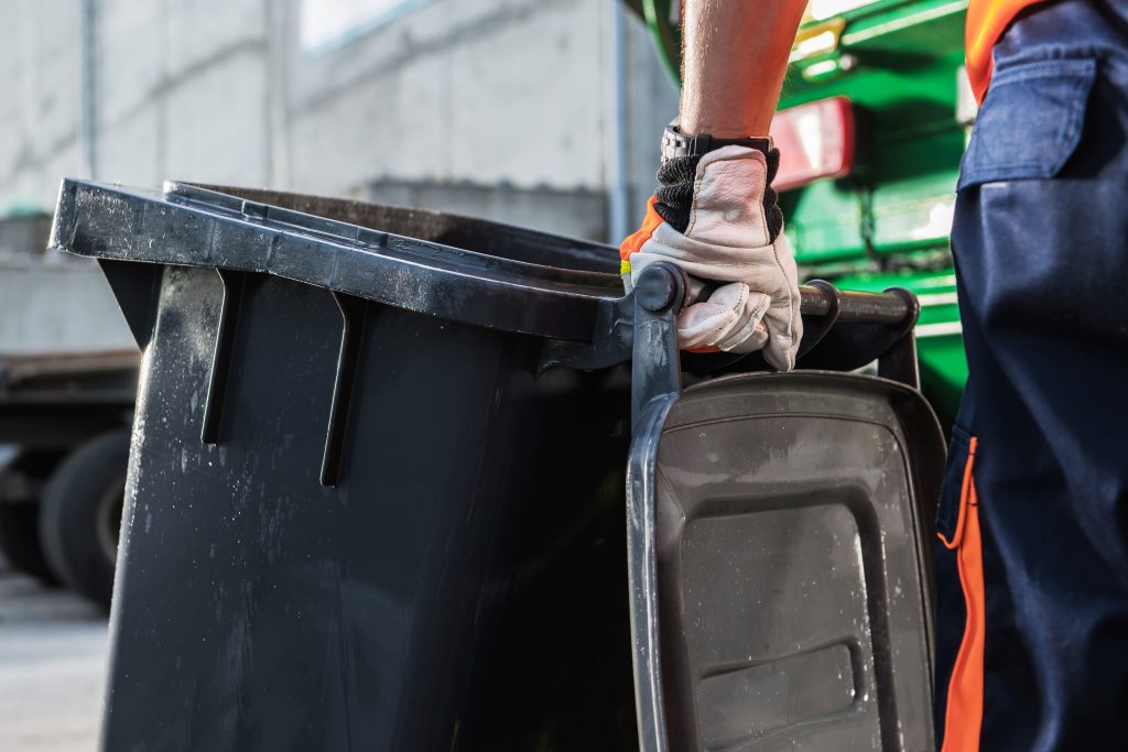 Garbage Disposal Worker Handles Trash Container Outdoors
