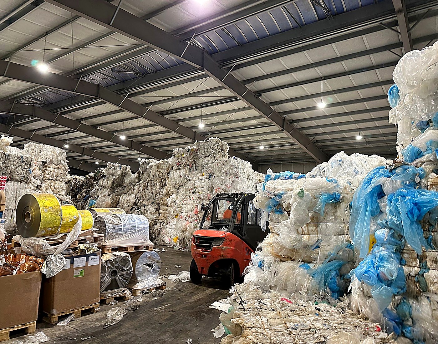 Forklift moving baled recyclable materials and film rolls through a material recovery facility warehouse