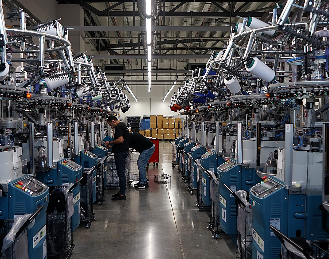 Worker inspecting a knitting machine on a textile production floor, representing manufacturer waste traceability at the source of production