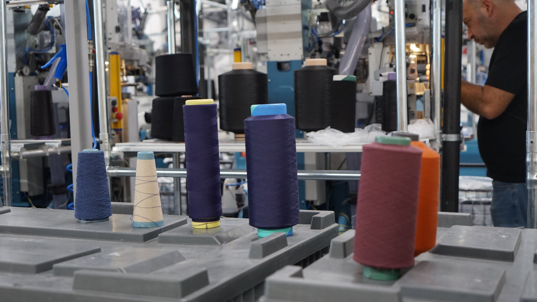 Worker inspecting a knitting machine on a textile production floor, representing manufacturer waste traceability at the source of production